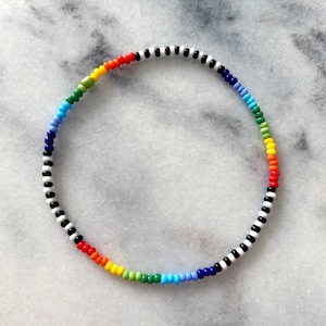 Könnte beinhalten: Ein Regenbogen-Perlenarmband mit schwarzen und weißen Perlen. Das Armband besteht aus kleinen, runden Perlen und ist auf einer dünnen, elastischen Schnur aufgefädelt.