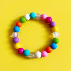 May include: A colorful beaded bracelet with alternating solid and clear beads. The beads are in a rainbow pattern, with red, orange, yellow, green, blue, indigo, and violet beads.