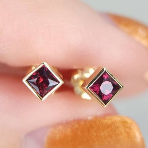May include: A pair of gold earrings with square-shaped red gemstones.