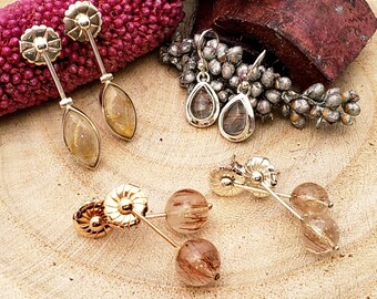 May include: A collection of gold-toned earrings with various designs. The earrings include teardrop, oval, and round shapes, all featuring a translucent, amber-colored stone with internal inclusions. The earrings are displayed on a wooden surface.