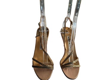 May include: A pair of gold and black strappy heeled sandals with a jeweled embellishment. The sandals are on a white background.