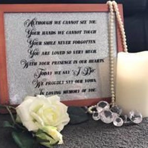 Pode incluir: Uma placa memorial enquadrada com fundo branco e texto preto. O texto diz: "Embora não possamos ver você, suas mãos não podemos tocar, seu sorriso nunca esquecido, você é muito amado, com sua presença em nossos corações, hoje dizemos sim, pronunciamos com orgulho nossos votos, em memória carinhosa de você."