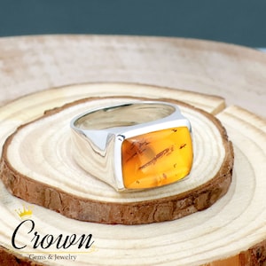 May include: A silver signet ring with a large, rectangular amber stone. The stone has a warm, honey-like color and is set in a polished silver band.