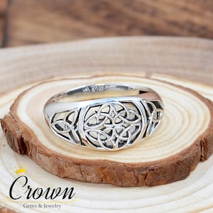 May include: A silver ring featuring a Celtic knot design. The ring is displayed on a wooden surface.