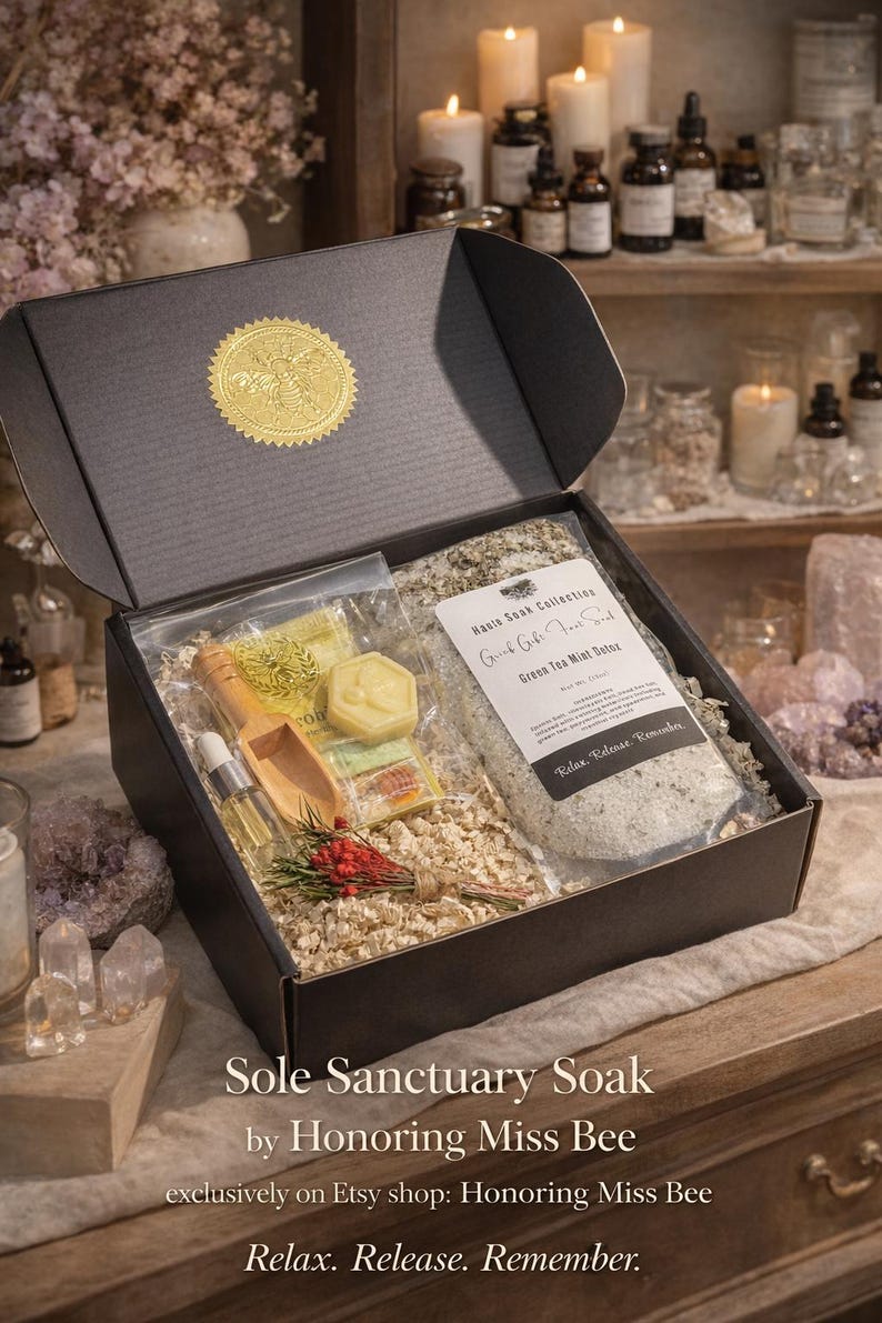 May include: A black gift box with a gold seal, filled with bath products. Includes a bag of Green Tea Mint Detox, a wooden scoop, a small bottle, and a bar of soap. The box is labeled "Sole Sanctuary Soak".
