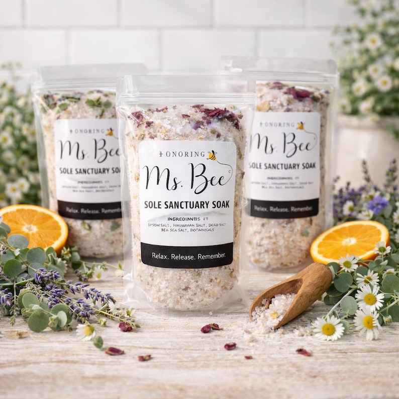 May include: Three clear bags of "Ms. Bee Sole Sanctuary Soak" with white labels and black text. The bags are filled with bath salts and botanicals. The image includes orange slices, flowers, and a wooden scoop.
