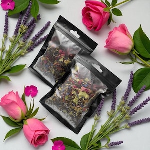 Può includere: Due sacchetti neri pieni di foglie di tè essiccate, circondati da rose rosa, rametti di lavanda e piccoli fiori rosa. Le foglie di tè sono un mix di colori, tra cui rosso, verde e blu.