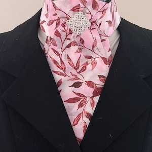 以下が含まれることがあります： ピンクとブラウンの模様のネクタイに、シルバーのラインストーンのピンが付いている。ネクタイは黒いスーツジャケットに合わせている。