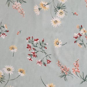 May include: A light sage green fabric featuring a repeating pattern of delicate wildflowers. The print includes clusters of white and yellow daisies, small red blossoms, and soft pink floral sprigs scattered across the smooth textile surface.