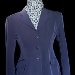 May include: A dark blue riding jacket with a white and black patterned scarf. The jacket has a classic design with a notched collar, four buttons, and two pockets.