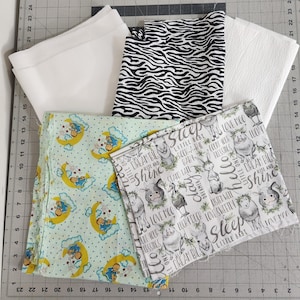 May include: Assortment of fabric pieces in various patterns. Includes white, black and white zebra print, and baby-themed fabrics with moons, stars, and animal illustrations. One fabric has the text "Sleep Little Baby".