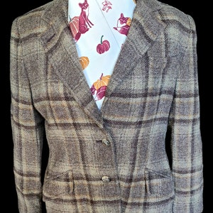 Puede incluir: Una chaqueta de cuadros marrón y beige con dos botones y dos bolsillos. La chaqueta se lleva sobre una corbata blanca con un estampado de zorros rojos, calabazas y setas.