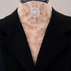 以下が含まれることがあります： 花柄の大きなラインストーンのブローチが付いたベージュのシルクネクタイ