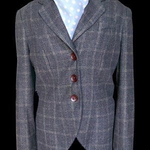 May include: A gray tweed blazer with a brown checkered pattern and four brown buttons. The blazer has a notched collar and a single vent in the back.