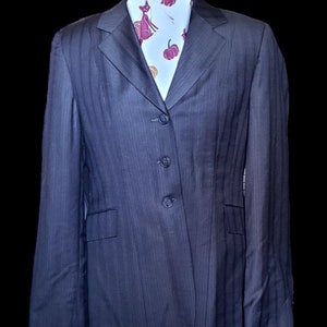 Puede incluir: Una chaqueta de traje gris oscuro con rayas finas y cuatro botones. La chaqueta tiene un corte clásico y está hecha de una tela de alta calidad.