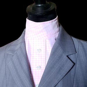 Op de afbeelding: Een grijze krijtstreepjas met een lichtroze en wit geruit overhemd. Het pak wordt gepresenteerd op een zwarte mannequin. De jas heeft een gekerfde revers en drie knopen.