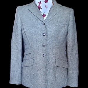 May include: A gray herringbone tweed blazer with a four-button closure. The blazer has two flap pockets on the front and a white patterned scarf with red accents.