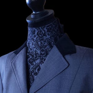 Peut inclure: Veste bleu foncé avec un col en velours noir et un ascot à motifs. L'ascot présente un motif floral noir. La veste a une fermeture à bouton noir unique et est présentée sur un mannequin noir.