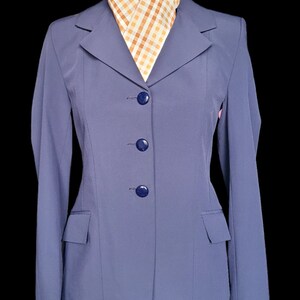 May include: A blue riding jacket with a white and orange checkered scarf. The jacket has a notched collar, three navy blue buttons, and a single pocket on the left side.