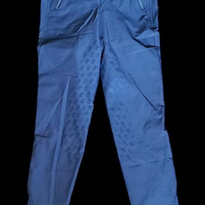 以下が含まれることがあります： 控えめなパターンとジッパー付きポケットが付いた青い乗馬用ズボンです。