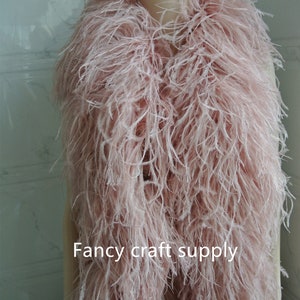 Op de afbeelding: Een roze struisvogelveren boa, een lange, pluche sjaal gemaakt van veren, op een wit mannequin. De boa is erg vol en zacht, en zou perfect zijn om een ​​toets van glamour toe te voegen aan elke outfit. De tekst "Fancy craft supply" is zichtbaar onderaan de afbeelding.