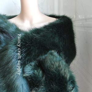 May include: A dark green faux fur shawl draped over a mannequin. The shawl is soft and fluffy, and it would be perfect for adding a touch of elegance to any outfit.