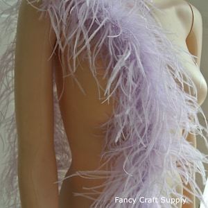 May include: A long, lavender ostrich feather boa. The boa is draped over a mannequin's shoulder and is very full and fluffy. The boa is a great addition to any costume or party outfit. "Fancy Craft Supply" is printed on the boa.