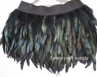 Pode incluir: Bordado de penas pretas com uma faixa elástica preta. As penas têm um brilho iridescente verde. "Fancy craft supply" está impresso no canto inferior direito da imagem.