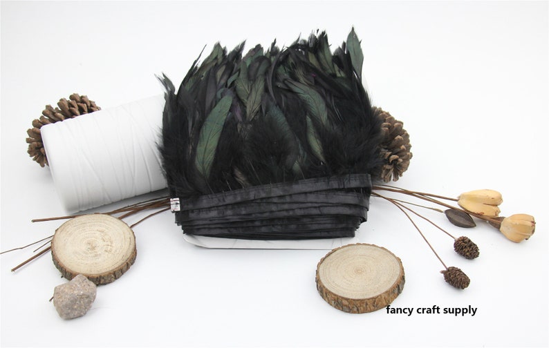 May include: Black feather trim with a green iridescent sheen. The trim is rolled up and tied with a black ribbon. The trim is on a white surface with wooden accents.