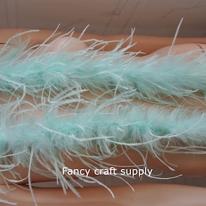 Op de afbeelding: Een lichtblauwe struisvogelveren boa. De boa is over een mannequin gelegd. De boa is zacht en pluche. "Fancy craft supply" is op de boa gedrukt.