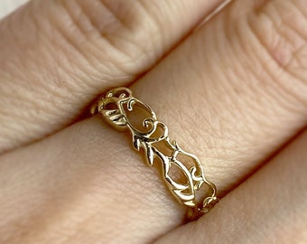 Könnte beinhalten: Ein zarter Goldring mit einem filigranen Design. Der Ring besteht aus einem dünnen Metallband mit filigranen Blumenmustern.
