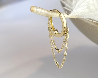 May include: Gold hoop earring with a delicate chain dangling from it. The chain is made of two strands of small, linked circles.