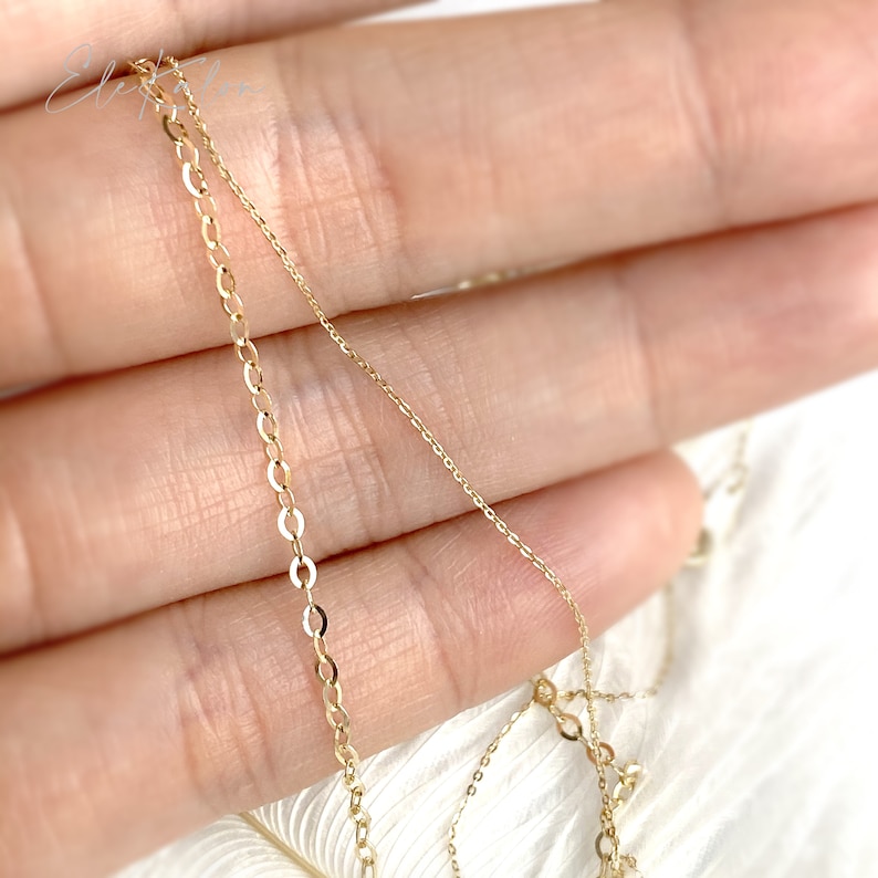 Op de afbeelding: Twee gouden kettingen, een delicate ketting en de andere een iets dikkere curb-ketting, worden getoond op een hand.
