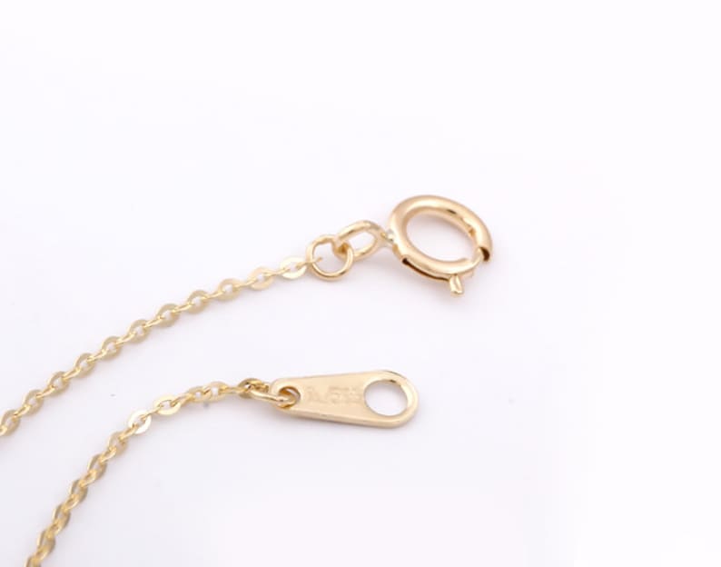 Op de afbeelding: Een gouden ketting met een karabijn sluiting en een veer sluiting. De ketting is gemaakt van kleine, ronde schakels.