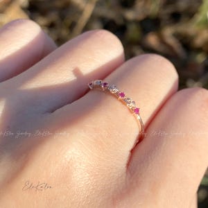 May include: A delicate gold band ring with a row of small pink gemstones set in rose-shaped designs.