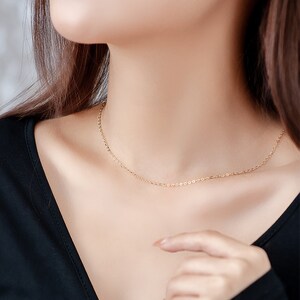 Op de afbeelding: Een delicate gouden kettingketting gedragen door een persoon met een zwart shirt.