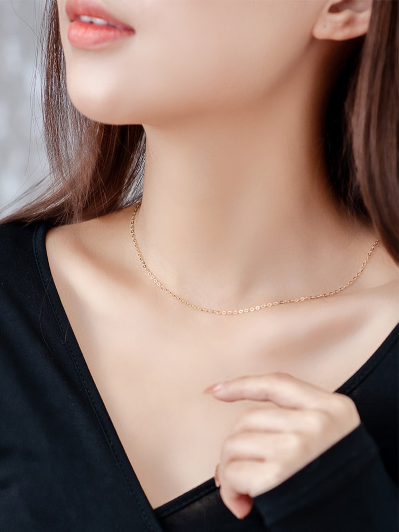 Op de afbeelding: Een delicate gouden kettingketting gedragen door een persoon met een zwart shirt.