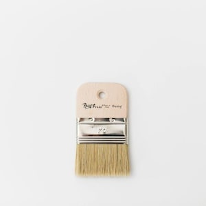 May include: A paint brush with a light wood handle and natural bristles. The handle has a hole for hanging and the text "Paint Pixie" and "Betty" printed on it. The metal ferrule is marked with the number "70".