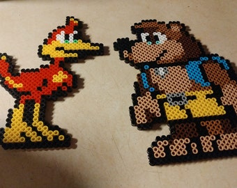 Può includere: Due personaggi di pixel art realizzati con perline colorate. Il personaggio a sinistra è un uccello rosso e giallo con un lungo becco. Il personaggio a destra è un orso bruno che indossa una camicia gialla e un gilet blu.