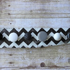 May include: A wooden board painted with a black and white chevron pattern. Five different black and white knobs are attached to the board.