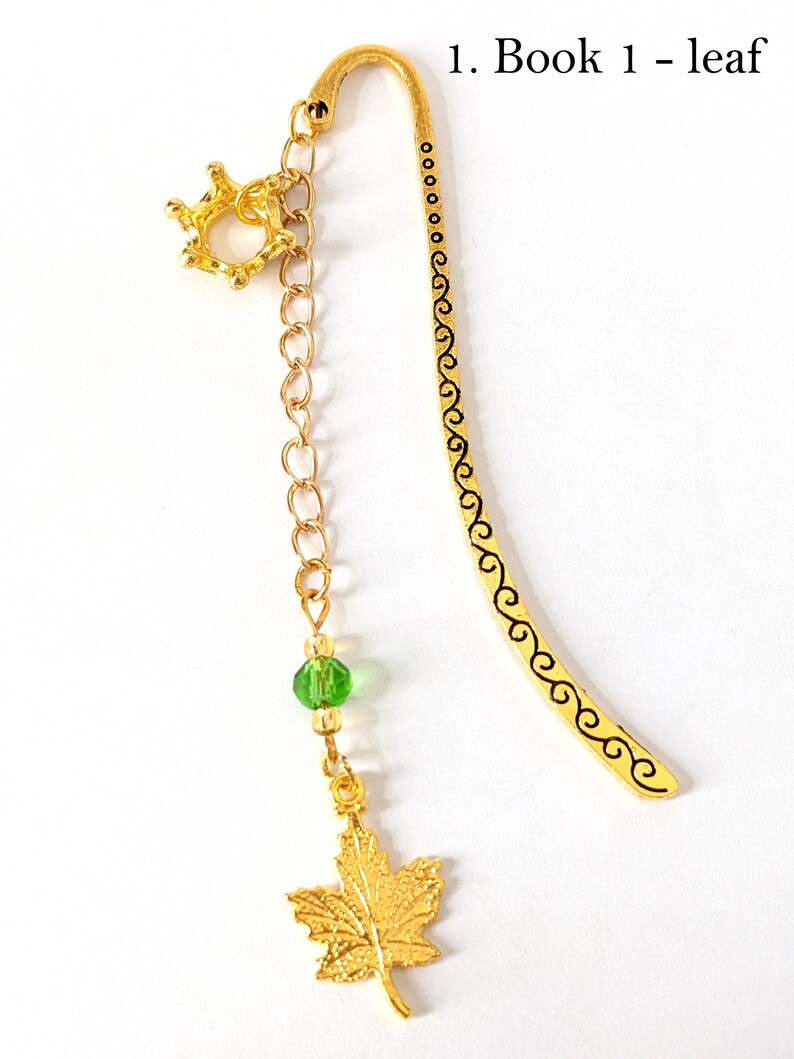 Puede incluir: Marcap&aacute;ginas dorado con un dije de hoja y una cuenta verde. El marcap&aacute;ginas tiene un acento en forma de corona y el texto "1. Book 1 - leaf". Dise&ntilde;ado para libros.