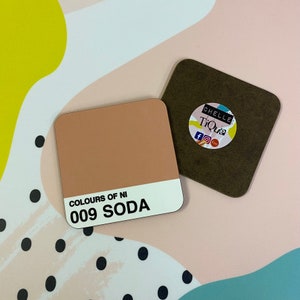 May include: Two square coasters, one brown and one light brown. The light brown coaster has the text "Colours of NI 009 SODA" printed on it. The brown coaster has a round sticker with the text "Chelle Tique" printed on it.
