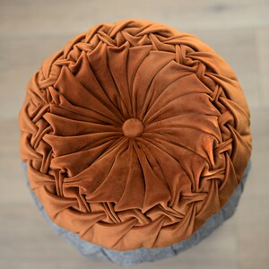 May include: A round, brown velvet cushion with a tufted design. The cushion has a circular button in the centre.