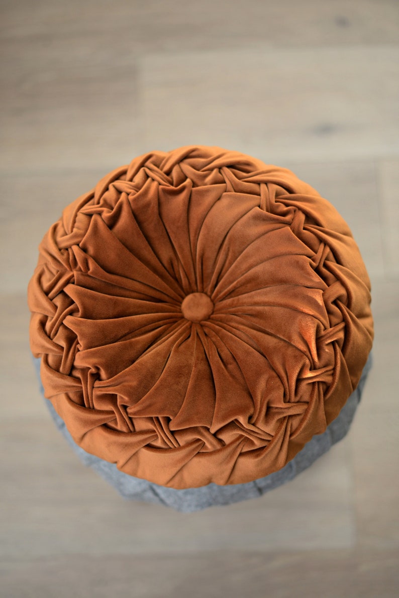 May include: A round, brown velvet cushion with a tufted design. The cushion has a circular button in the centre.