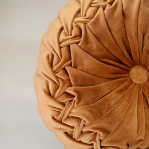 May include: A round, brown velvet cushion with a tufted design. The cushion has a button in the centre.