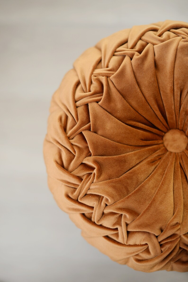 May include: A round, brown velvet cushion with a tufted design. The cushion has a button in the centre.
