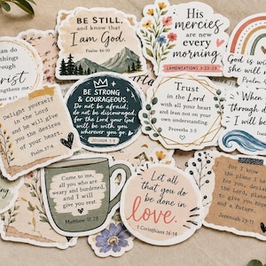 May include: A collection of die-cut vinyl stickers featuring various religious quotes and scripture verses. The designs include floral accents, a rainbow, a coffee mug, and mountain illustrations with text such as Be Still, His Mercies, and Trust in the Lord.