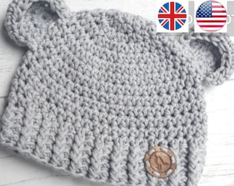 May include: A light grey crocheted hat with bear ears. The hat has a ribbed brim and a small, round, wooden button with a bird design. The text "_YARNIYROBIN" is visible at the bottom of the image.