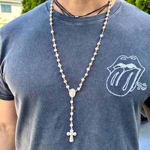 Könnte beinhalten: Eine silberne, goldene und roségoldene Rosenkranz Halskette mit einem silbernen Kreuz und einem silbernen Anhänger mit einem religiösen Bild.