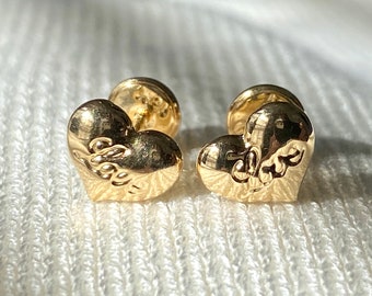 May include: A pair of gold heart-shaped earrings with the word "love" engraved on each heart.